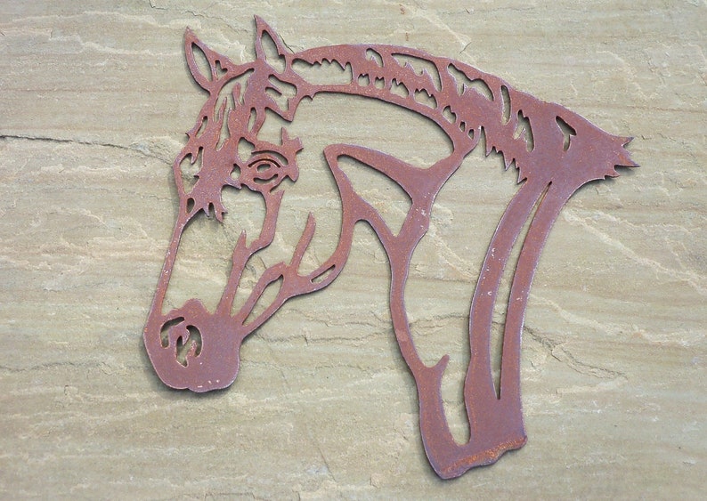 Puede incluir: Una decoraci&oacute;n de pared de metal oxidado en forma de silueta de cabeza de caballo. La cabeza del caballo est&aacute; mirando hacia el lado derecho de la imagen. El metal es de color marr&oacute;n oscuro con una textura rugosa.