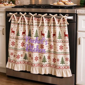 Peut inclure: Un torchon de four couleur crème avec un motif festif de rennes rouges, de sapins verts et de flocons de neige rouges. Le torchon présente un bord inférieur à volants, six attaches en tissu en haut et le texte brodé violet Rachel's Kitchen.