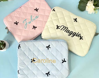 May include: Three quilted laptop cases in pastel colors: pink, yellow, and light blue. Each case features a diamond pattern, black bow accents, and a name embroidered in a contrasting color: "Julia", "Maggie", and "Caroline".