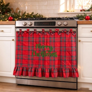 Op de afbeelding: Een ovenhoes van rood en groen geruite stof met een geplooide onderrand en zeven kleine stoffen strikjes aan de bovenkant. De tekst Merry Christmas is in groene cursieve letters in het midden van het stoffen paneel geborduurd.