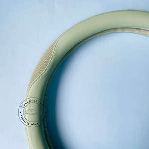 Peut inclure: Un couvre-volant de couleur vert clair avec un motif textur&eacute;. Le couvre-volant comporte un logo noir et blanc qui dit "Done Art Craft Steering Wheel Cover".