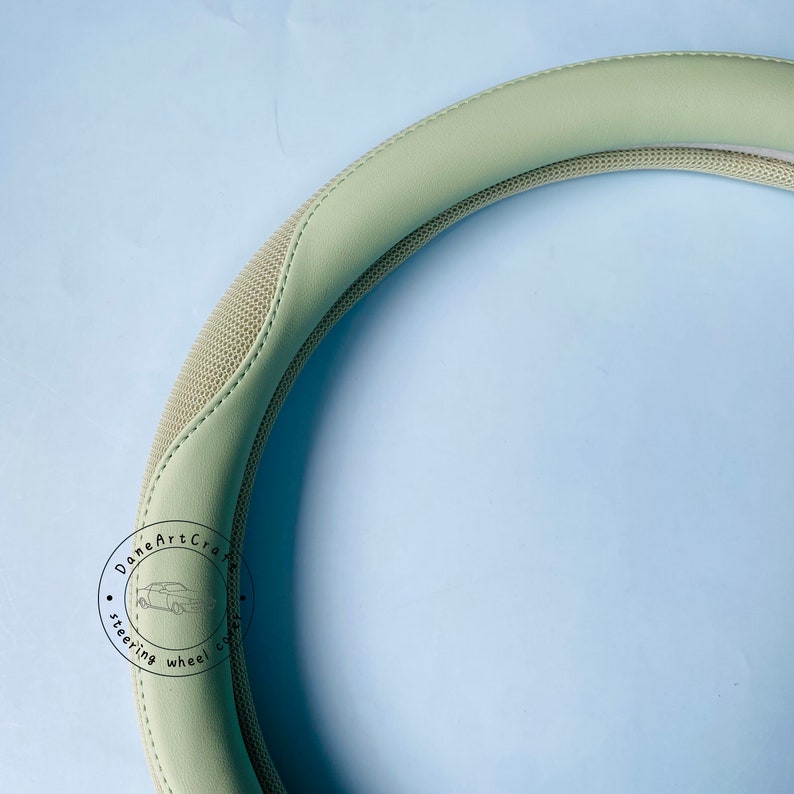 Peut inclure: Un couvre-volant de couleur vert clair avec un motif textur&eacute;. Le couvre-volant comporte un logo noir et blanc qui dit "Done Art Craft Steering Wheel Cover".