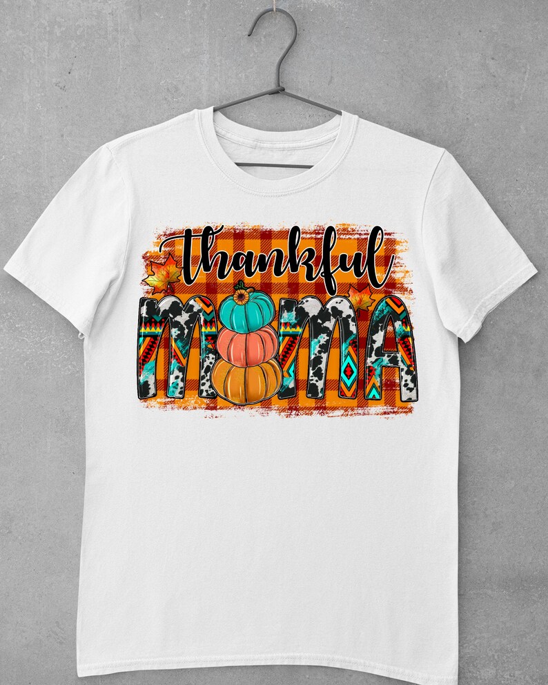 K&ouml;nnte beinhalten: Wei&szlig;es T-Shirt mit dem Text "Thankful Mama" in schwarz-wei&szlig;en Buchstaben auf kariertem Hintergrund. Der Text ist mit Herbstbl&auml;ttern und K&uuml;rbissen verziert.