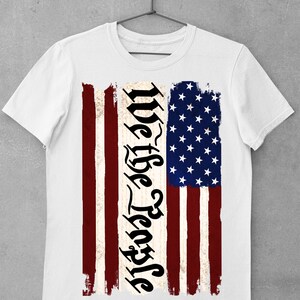 Peut inclure: T-shirt blanc avec un motif de drapeau am&eacute;ricain vieilli et le texte "We the People" imprim&eacute; verticalement sur le c&ocirc;t&eacute; gauche du drapeau.