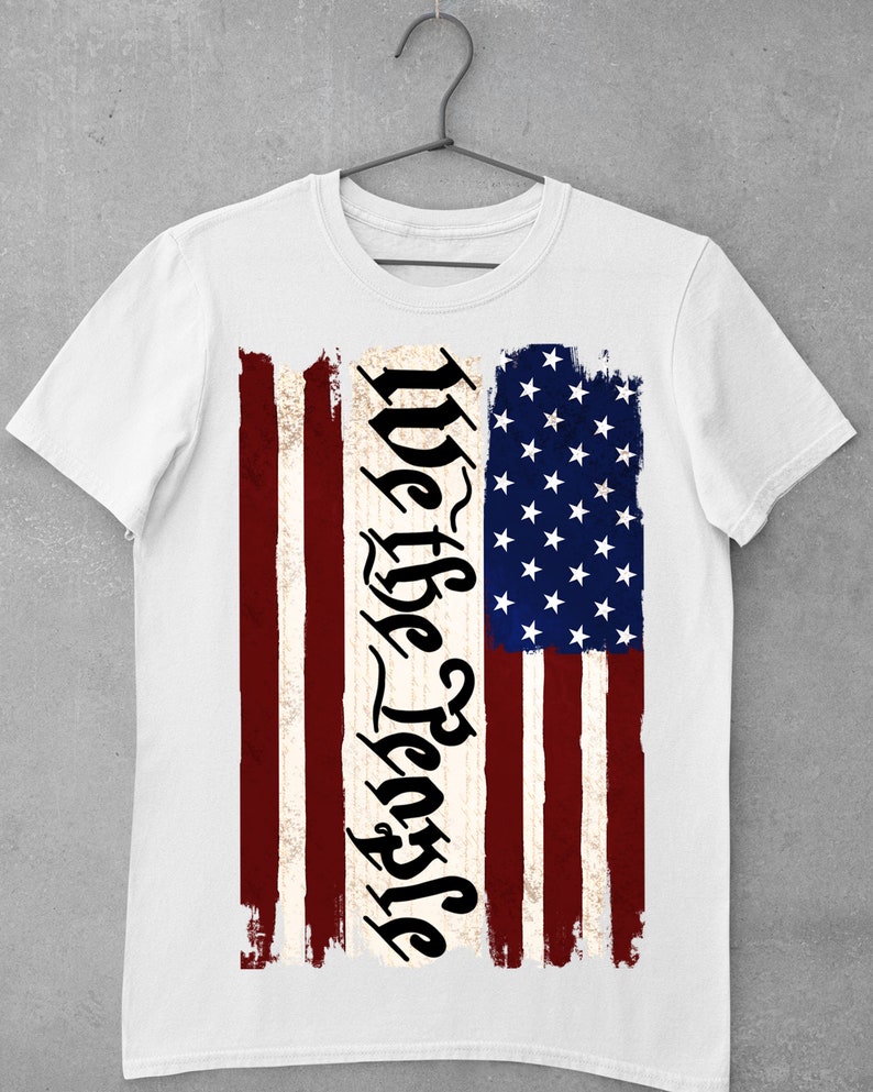 Peut inclure: T-shirt blanc avec un motif de drapeau am&eacute;ricain vieilli et le texte "We the People" imprim&eacute; verticalement sur le c&ocirc;t&eacute; gauche du drapeau.