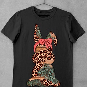 May include: Black t-shirt with a graphic of a brown and orange leopard print bunny with a pink bow. The bunny is sitting on a wooden background with a turquoise floral pattern.