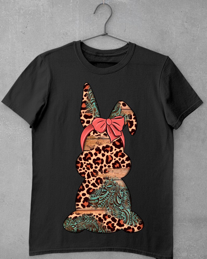 May include: Black t-shirt with a graphic of a brown and orange leopard print bunny with a pink bow. The bunny is sitting on a wooden background with a turquoise floral pattern.