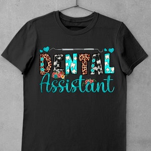 Op de afbeelding: Zwart T-shirt met de tekst "Dental Assistant" in turquoise blauwe letters met een tandheelkundig gereedschap en harten boven de tekst. De letters zijn versierd met verschillende patronen, waaronder luipaardprint, koe-print en tandvormen.