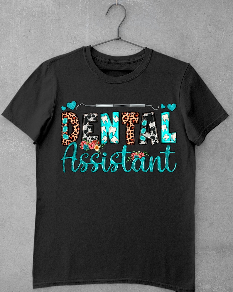 Op de afbeelding: Zwart T-shirt met de tekst "Dental Assistant" in turquoise blauwe letters met een tandheelkundig gereedschap en harten boven de tekst. De letters zijn versierd met verschillende patronen, waaronder luipaardprint, koe-print en tandvormen.