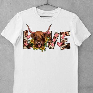 May include: White t-shirt featuring a graphic of a Highland cow with a floral wreath around its head. The word "LOVE" is spelled out in large letters with a leopard print and pink hearts.