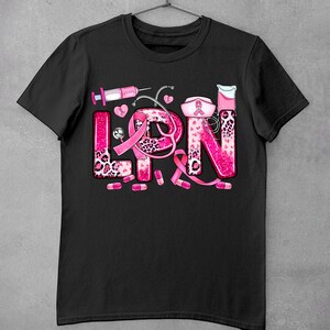 May include: Black t-shirt with a pink and white design that says "LPN" with a pink ribbon, stethoscope, pills, and other medical symbols.