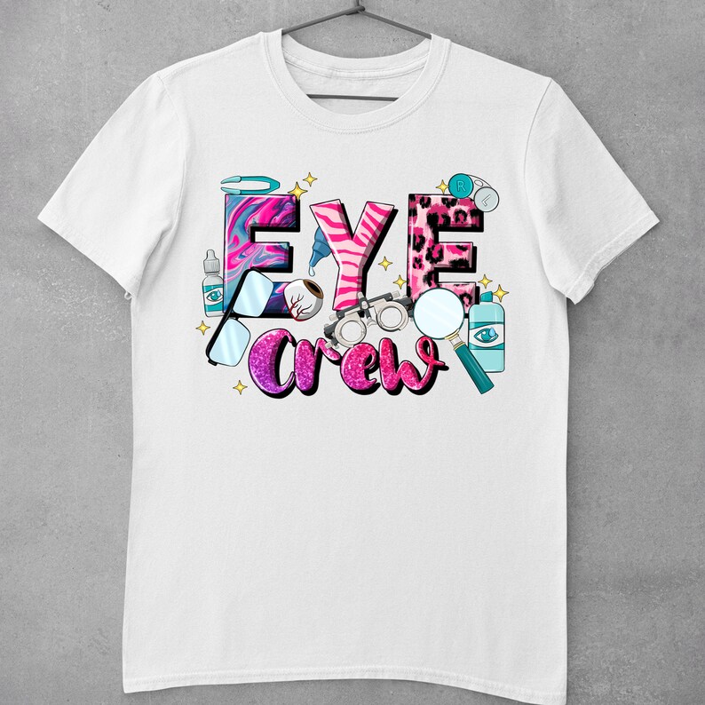 May include: White t-shirt with a pink, blue, and black graphic design that says "Eye Crew". The graphic includes images of an eye, glasses, and other eye-related objects.