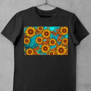 May include: Black t-shirt featuring a vibrant sunflower design. The graphic showcases yellow sunflowers with brown centers against a teal and brown patterned background. The shirt is hanging on a metal hanger.