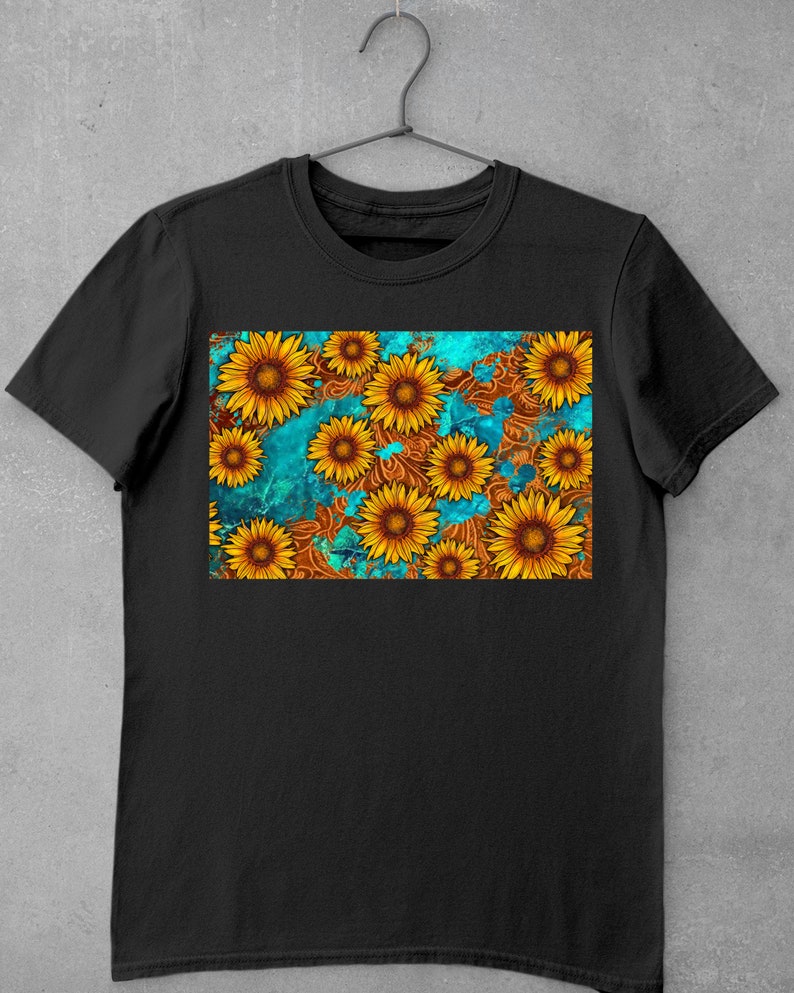 May include: Black t-shirt featuring a vibrant sunflower design. The graphic showcases yellow sunflowers with brown centers against a teal and brown patterned background. The shirt is hanging on a metal hanger.