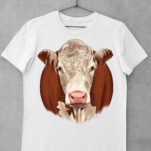 May include: White t-shirt featuring a detailed illustration of a Hereford cow's face. The cow has a white face with brown markings around the eyes and ears, and a pink nose. The artwork is set against a brown background.