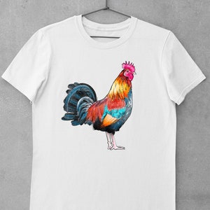 May include: White t-shirt with a colorful rooster illustration. The rooster is facing right and has a red, orange, yellow, blue, and black color scheme.