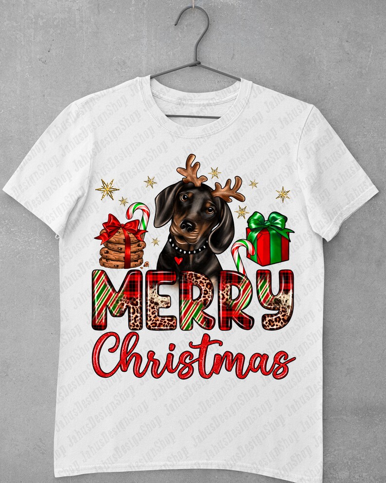 May include: A white t-shirt with a black and brown dachshund wearing a red and green plaid Santa hat with antlers. The dog is holding a candy cane and a gift box. The text "Merry Christmas" is written in red and green plaid with leopard print accents.