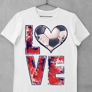 Puede incluir: Camiseta blanca con un gr&aacute;fico "LOVE" desgastado en rojo, blanco y azul. La "O" se reemplaza con un bal&oacute;n de f&uacute;tbol en forma de coraz&oacute;n.