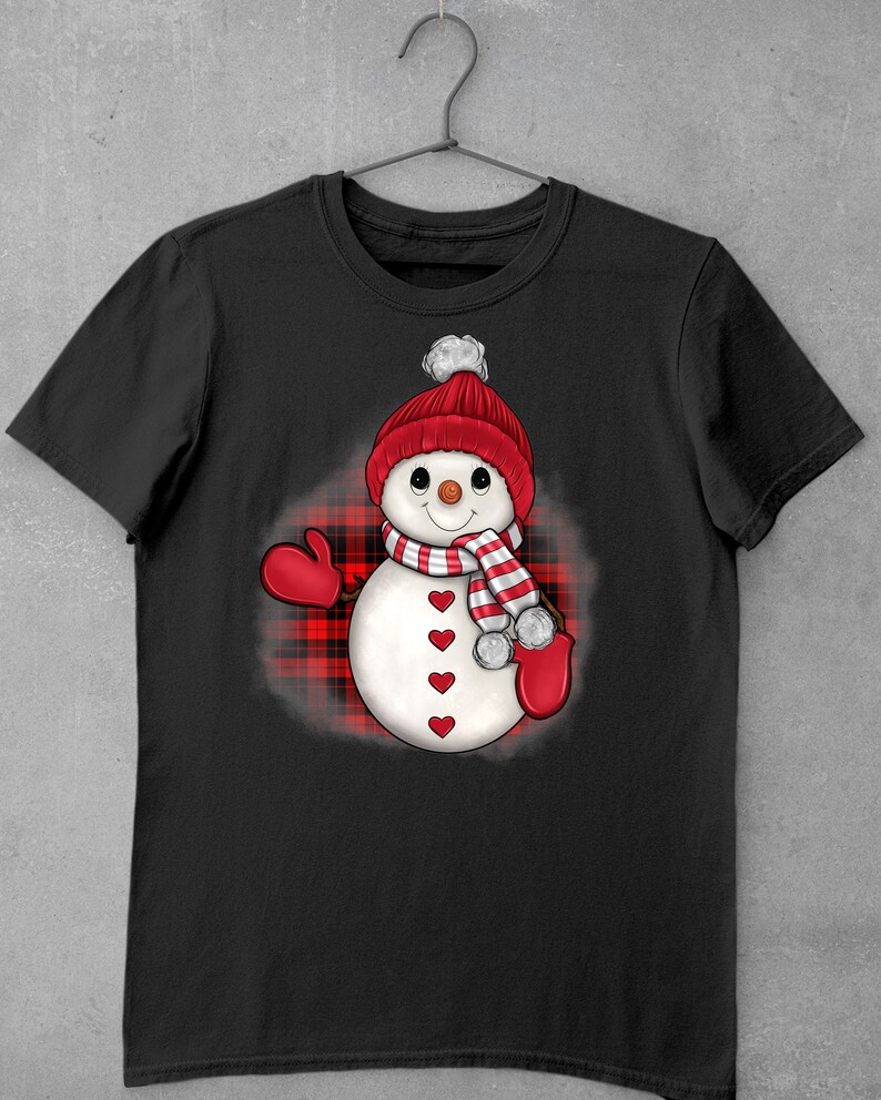 May include: Black t-shirt with a snowman design. The snowman is wearing a red knitted hat with a white bobble, a striped scarf, and red mittens. The snowman's body has red heart accents. The design is set against a red and black plaid background.
