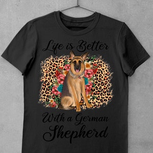 May include: Black t-shirt with a German Shepherd dog sitting on a leopard print background with flowers. The text "Life is Better With a German Shepherd" is printed on the shirt.