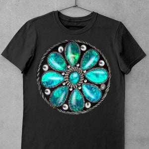 Op de afbeelding: Zwart T-shirt met een cirkelvormig ontwerp in turquoise en zilver met een bloemvormig patroon met meerdere turquoise stenen.