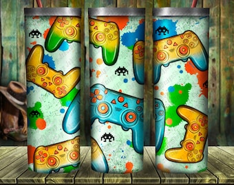 May include: Three colorful stainless steel tumblers with a repeating pattern of video game controllers and space invaders. The background is a white canvas with splashes of blue, green, orange, and red paint.