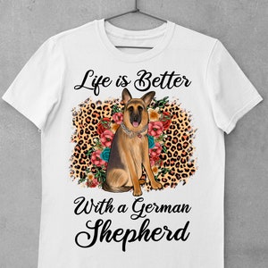 May include: White t-shirt with a German Shepherd dog sitting in a leopard print and floral design. The text "Life is Better with a German Shepherd" is printed on the shirt.