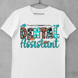 Op de afbeelding: Wit T-shirt met een turquoise ontwerp met de tekst "Dental Assistant". Het ontwerp bevat een tandheelkundig instrument, harten en dierenprintpatronen.