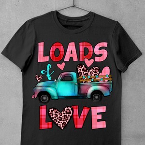 May include: Black t-shirt featuring a teal and pink vintage truck carrying leopard print hearts. The words "LOADS of LOVE" are in pink and red plaid lettering. Small pink hearts are scattered around the truck design.