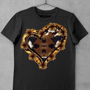 Puede incluir: Camiseta negra con un dise&ntilde;o en forma de coraz&oacute;n que presenta un estampado de animal marr&oacute;n y negro rodeado por un borde de purpurina dorada y girasoles.