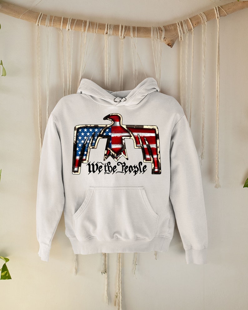 May include: White hooded sweatshirt with a graphic of an eagle with the American flag design and the text "We the People".