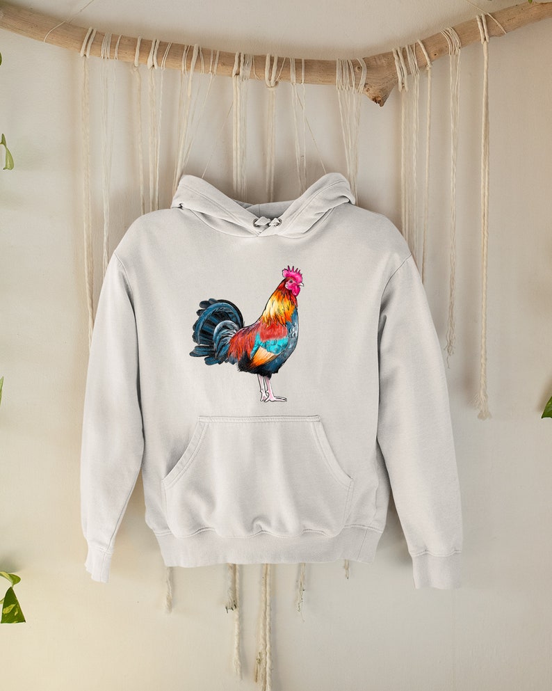 May include: A white hoodie with a colorful rooster illustration on the front. The rooster has a red comb, yellow and orange feathers, and blue and black tail feathers.