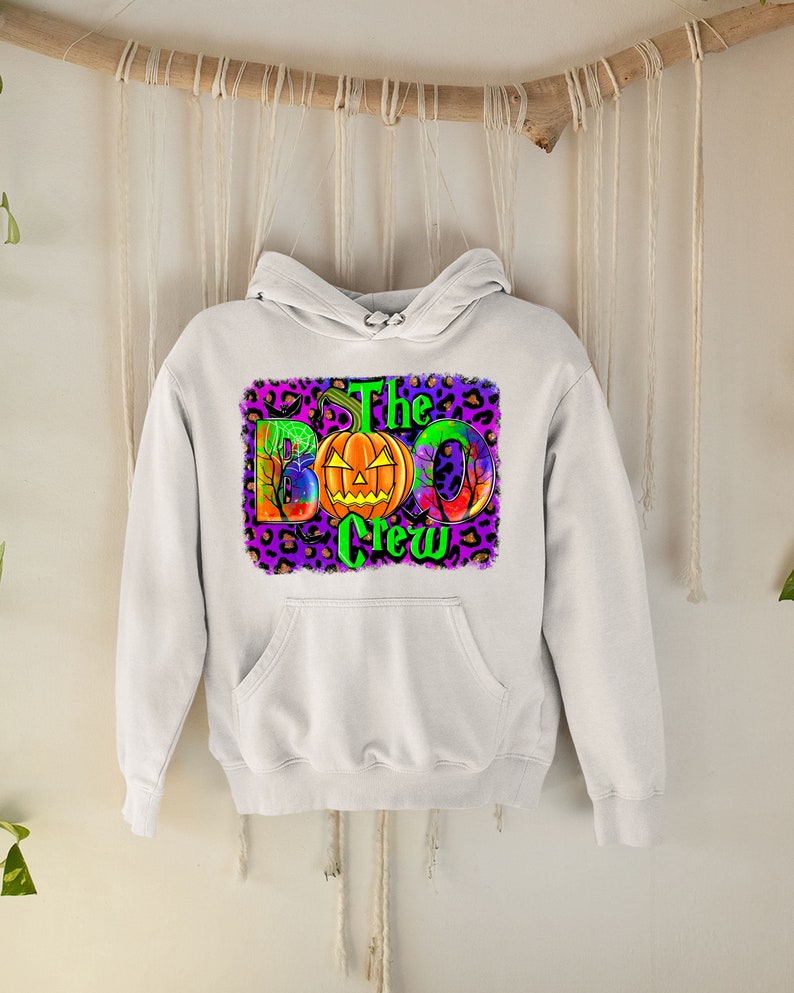May include: White hooded sweatshirt with a graphic print of a pumpkin and the text "The Boo Crew" on a purple and leopard print background.