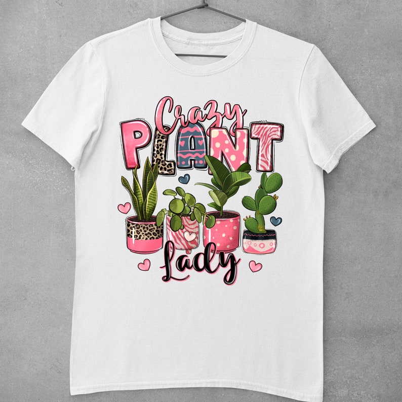 Pu&ograve; includere: Maglietta bianca con un design grafico rosa e nero che dice "Crazy Plant Lady" con una variet&agrave; di piante in vaso in vasi rosa.