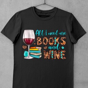 May include: Black t-shirt with a graphic design of a glass of red wine and a stack of books. The text "All I need are BOOKS and WINE" is written in turquoise letters on a leopard print background.