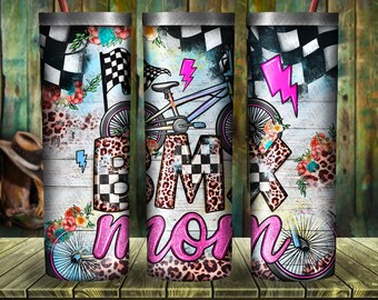 May include: A white tumbler with a pink, black, and white BMX bike design. The tumbler has a checkered pattern, leopard print, and floral accents. The text "BMX mom" is written in pink glitter letters.