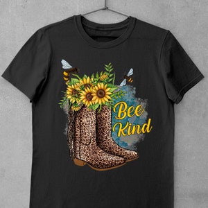 May include: Black t-shirt with a graphic of a pair of leopard print cowboy boots with sunflowers and bees. The text "Bee Kind" is written in white letters.