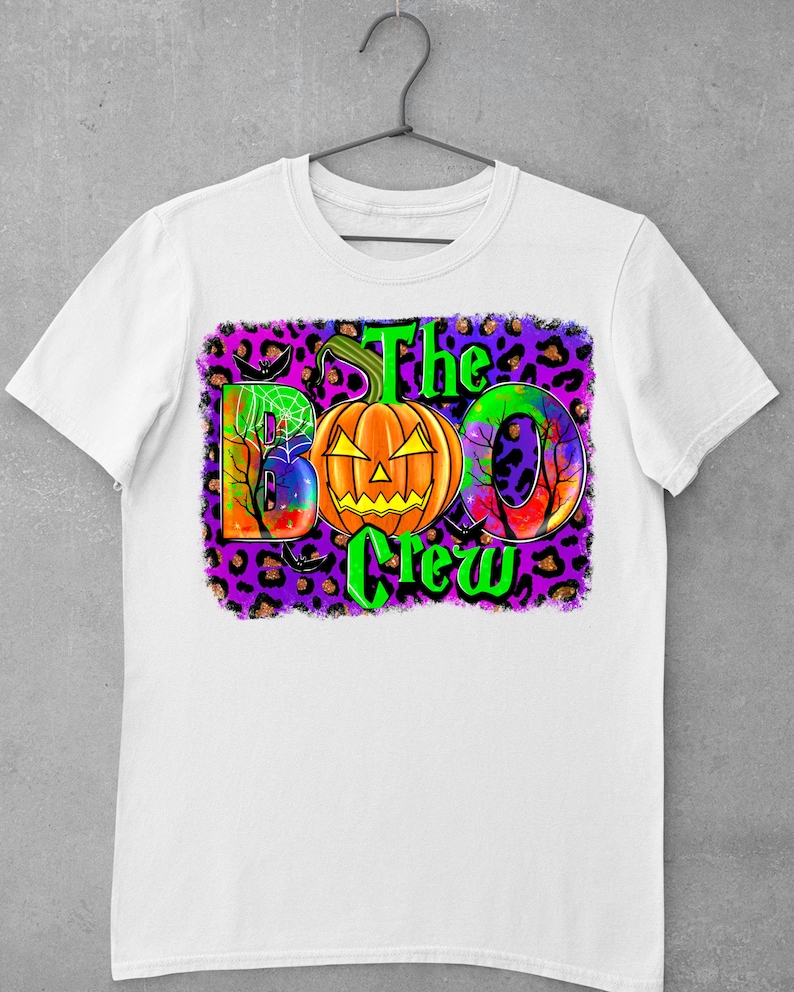 May include: White t-shirt with a colourful graphic design featuring a pumpkin, the words "The Boo Crew", and a leopard print background.