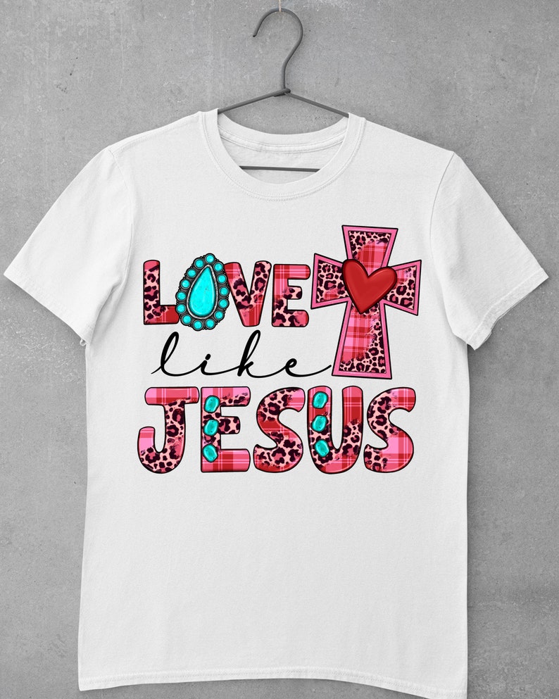 May include: White t-shirt with a pink, red, and black leopard print design that says "Love like Jesus" with a turquoise jewel and a red heart on a pink and black cross.