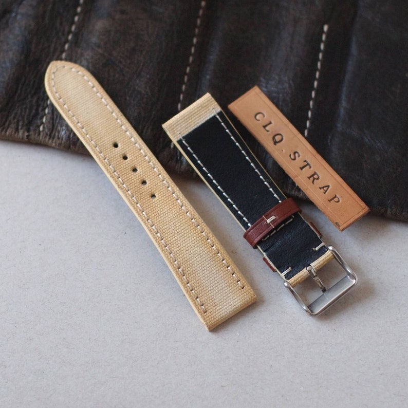 May include: A collection of watch straps in various styles. One strap is beige canvas with white stitching, another is black and beige with a brown leather accent, and a third is a leather tag with the text "CLQ. STRAP".