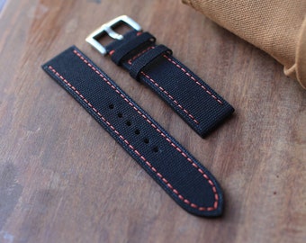 May include: Two black watch straps with red stitching. The straps are made of a woven fabric and have a buckle closure.
