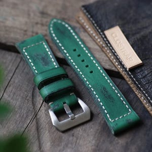 May include: Two green leather watch straps with white stitching. The strap on the left has a buckle. The strap on the right has the word "CLOSTRAP" embossed on it.