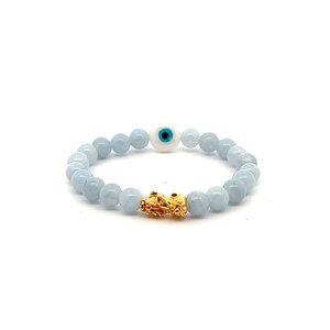 May include: A light blue beaded bracelet with a gold charm and a white evil eye bead with a blue center.