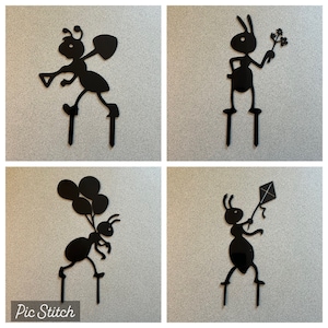 May include: Four black silhouette ant cake toppers. Each ant is standing on two legs and holding a different object. The first ant is holding a shovel, the second ant is holding a flower, the third ant is holding balloons, and the fourth ant is holding a kite.