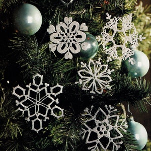 May include: Five white crocheted snowflakes hanging on a green Christmas tree with blue ornaments.