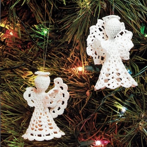 Puede incluir: Dos adornos de ángel de crochet blanco colgados de un árbol de Navidad con luces de colores.