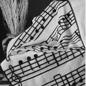 Könnte beinhalten: Schwarz-weiße Häkeldecke mit Noten-Design. Die Decke hat ein sich wiederholendes Muster aus Violinschlüsseln und Noten.