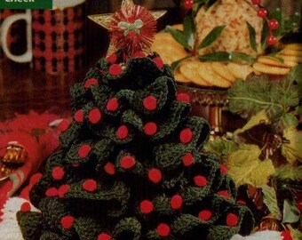 May include: A handmade, crocheted Christmas tree with red ornaments and a star topper. The tree is dark green with red accents and sits on a white and red crocheted base. A festive holiday decoration.