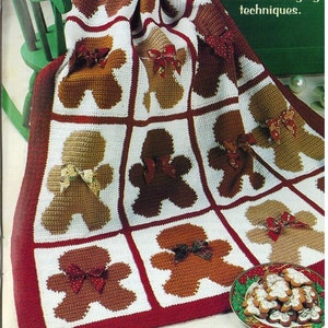 May include: A crocheted blanket featuring a gingerbread man design in brown, white and red. The blanket is folded on a chair with a plate of gingerbread cookies in the foreground. The text "See Crochet Coach on page 8 for colour changing techniques." is visible in the top right corner.