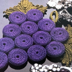 Puede incluir: Un posavasos de ganchillo con diseño de uva, con una hoja verde y uvas moradas. Las uvas están en racimo y están hechas de hilo.